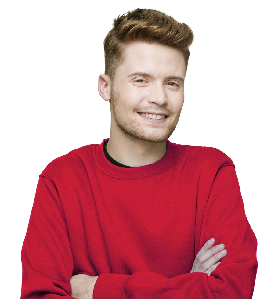 A young man wearing a red jumper stands smiling with crossed arms